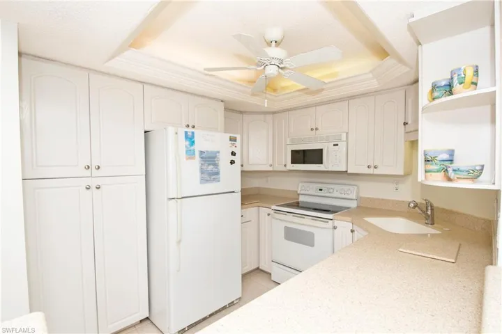 Kitchen with white cabinetry, sink, white appliances, and a tray ceiling