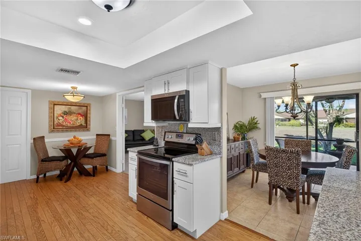 Kitchen with stainless steel appliances, white cabinetry, backsplash, decorative light fixtures, and light stone counters