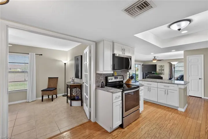 Kitchen featuring appliances with stainless steel finishes, white cabinetry, light stone counters, light wood-style floors, and tasteful backsplash