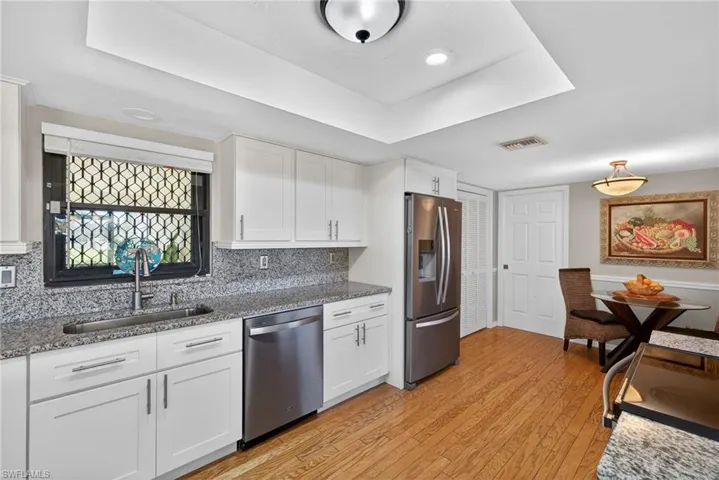 Kitchen featuring white cabinets, appliances with stainless steel finishes, dark stone counters, and light wood-style flooring