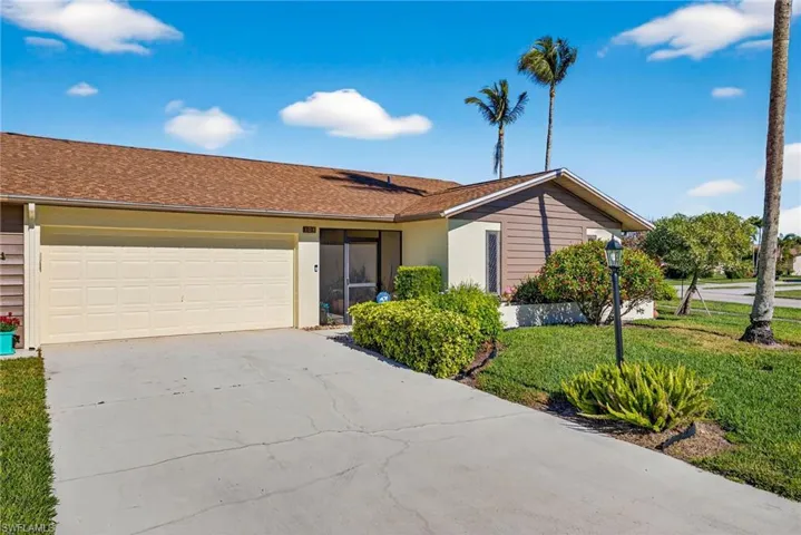 Ranch-style home featuring concrete driveway, an attached garage, a front lawn, and roof with shingles