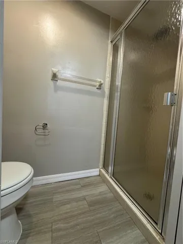 Bathroom featuring wood-type flooring, a shower with shower door, and toilet