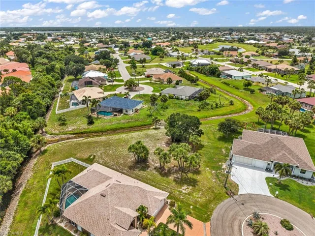 Aerial perspective showcasing multiple properties with screened pools, lush green lawns, mature palm trees, and cul-de-sac street designs
