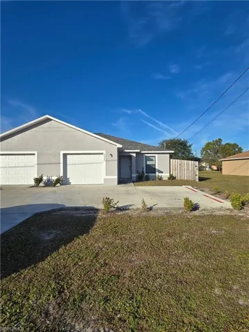Duplex featuring stucco siding, concrete driveway, a front lawn, and a garage