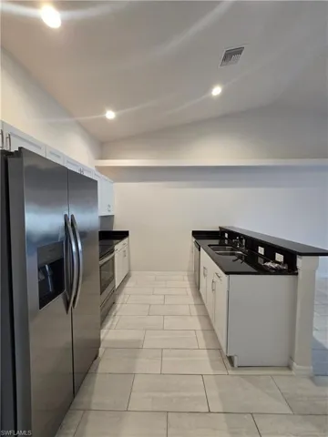 Kitchen with appliances with stainless steel finishes, white cabinetry, lofted ceiling, and recessed lighting