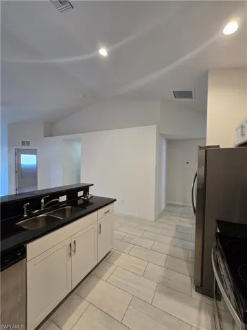 Kitchen featuring white cabinetry, stainless steel appliances, lofted ceiling, recessed lighting, and dark stone countertops