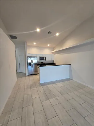Kitchen featuring vaulted ceiling, dark countertops, a peninsula, stainless steel appliances, and white cabinets