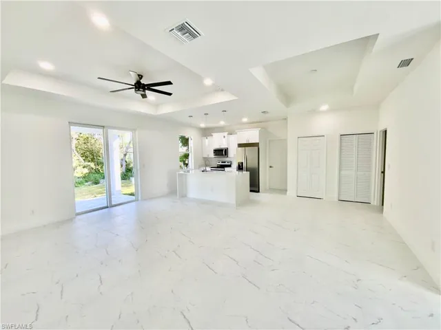 Unfurnished living room with a tray ceiling, light tile patterned floors, sink, and ceiling fan