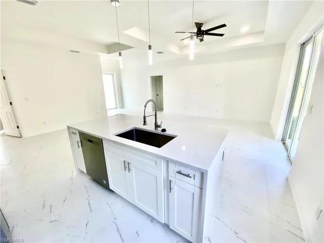 Kitchen featuring a raised ceiling, stainless steel dishwasher, white cabinetry, ceiling fan, and sink