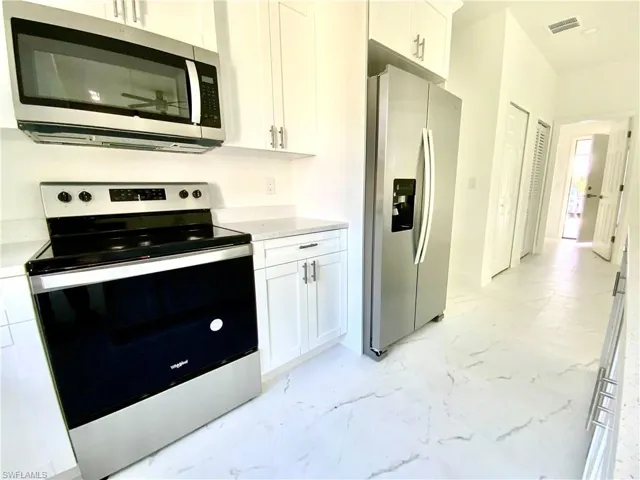 Kitchen with white cabinets, stainless steel appliances, and light stone countertops