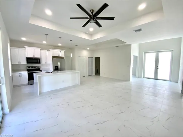 Kitchen with appliances with stainless steel finishes, light tile patterned flooring, a tray ceiling, and a center island with sink