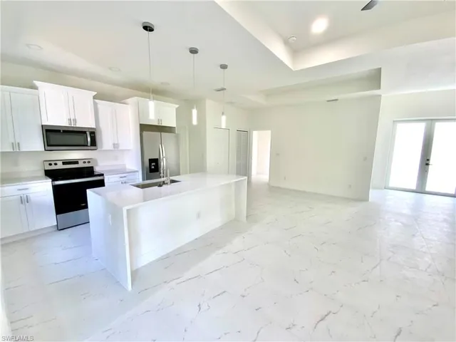 Kitchen with a kitchen island with sink, light tile patterned floors, a tray ceiling, stainless steel appliances, and sink