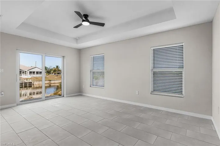 Unfurnished room with a tray ceiling, ceiling fan, a water view, and light tile patterned floors