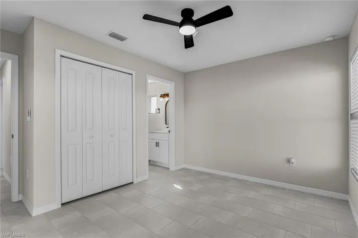 Unfurnished bedroom featuring a closet, a ceiling fan, ensuite bathroom, and light tile patterned floors
