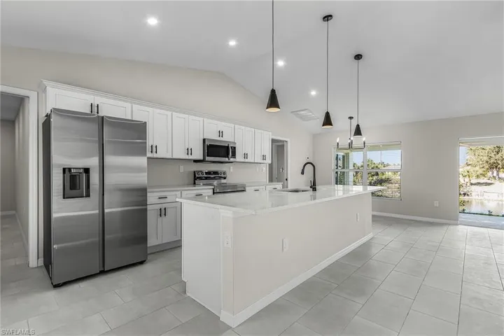Kitchen with appliances with stainless steel finishes, white cabinets, light stone countertops, a center island with sink, and decorative light fixtures