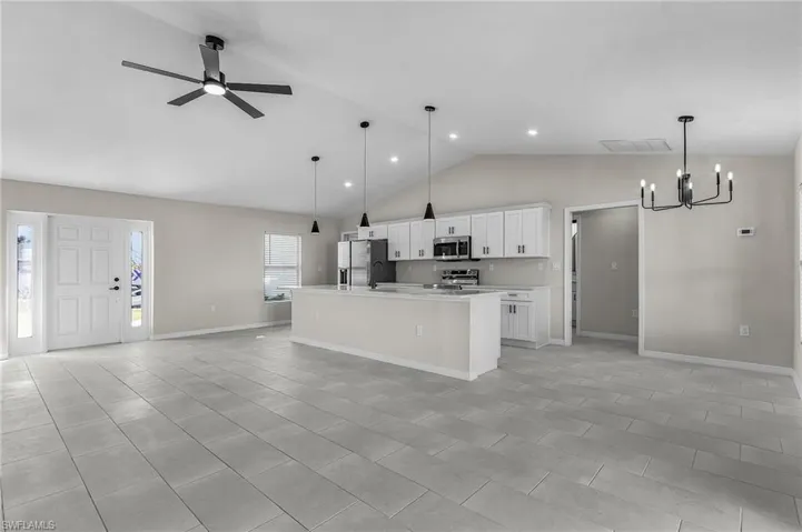 Kitchen with open floor plan, white cabinets, hanging light fixtures, high vaulted ceiling, and a chandelier