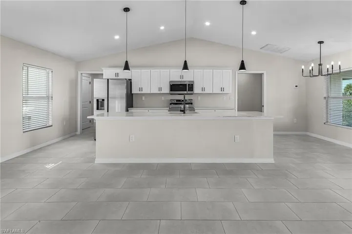 Kitchen featuring white cabinetry, appliances with stainless steel finishes, hanging light fixtures, a large island, and lofted ceiling