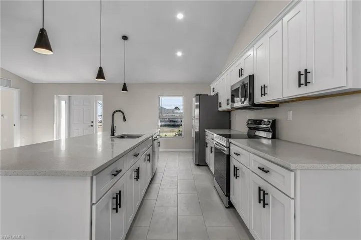 Kitchen with lofted ceiling, appliances with stainless steel finishes, a large island with sink, pendant lighting, and white cabinets