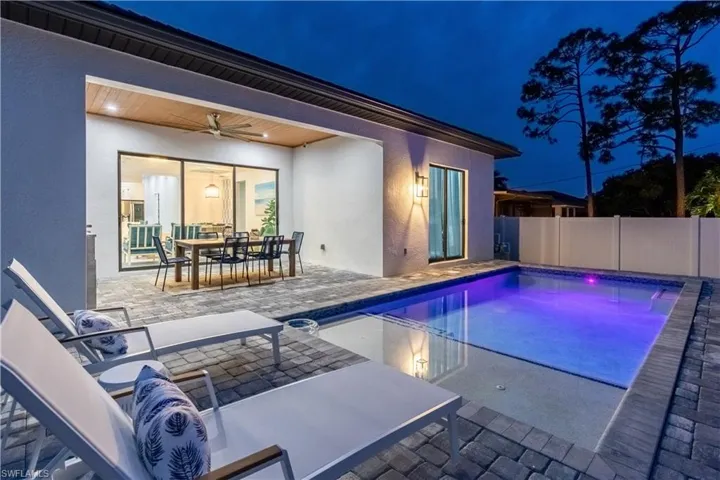 Pool at night with outdoor dining area, a patio, and a fenced backyard