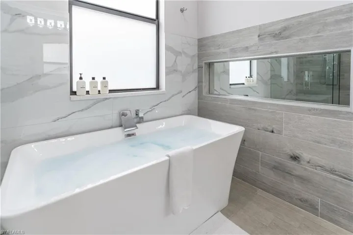 Full bath featuring a freestanding tub, tile walls, and a marble finish shower