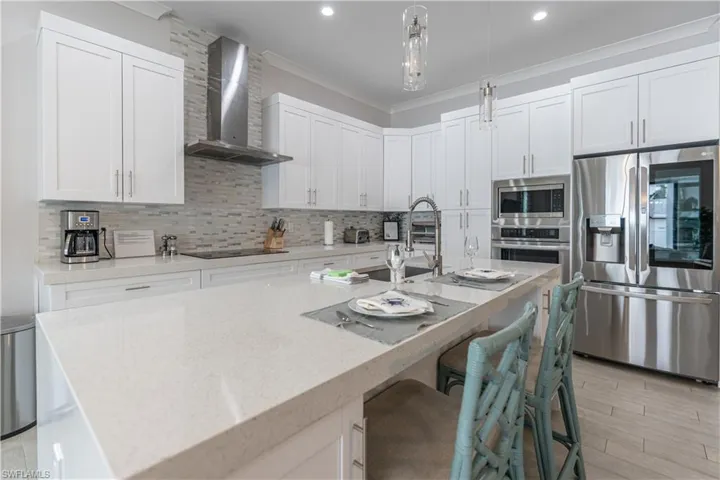 Kitchen featuring stainless steel appliances, backsplash, light stone counters, white cabinets, and hanging light fixtures