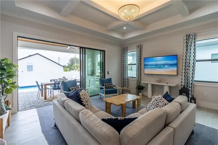 Living area featuring coffered ceiling, beamed ceiling, a sunroom, ceiling fan, and a chandelier