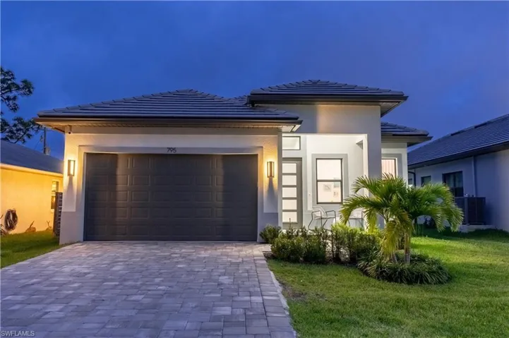 Prairie-style home featuring decorative driveway, an attached garage, a tiled roof, and a lawn