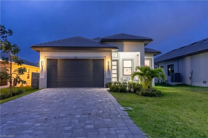 Prairie-style home with a yard, decorative driveway, an attached garage, stucco siding, and a tile roof