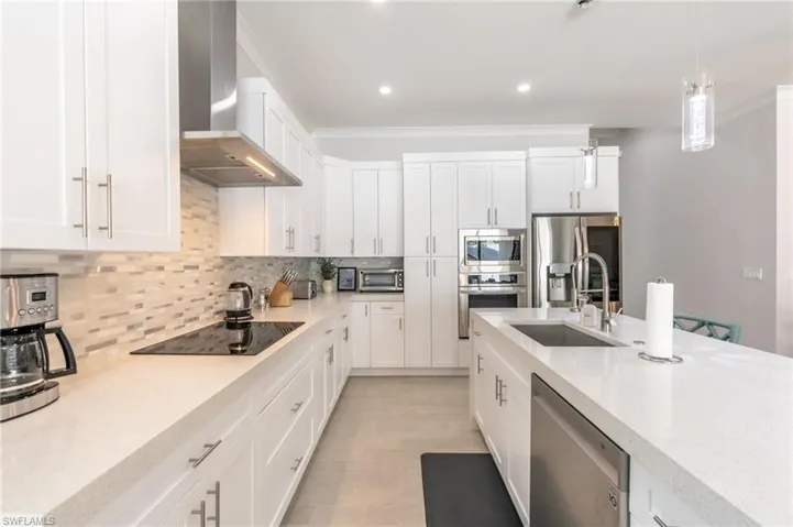 Kitchen with white cabinetry, wall chimney exhaust hood, appliances with stainless steel finishes, pendant lighting, and recessed lighting
