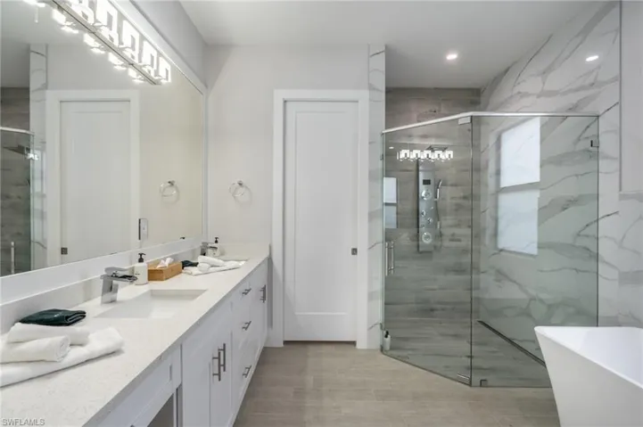 Full bath with double vanity, a marble finish shower, and a soaking tub