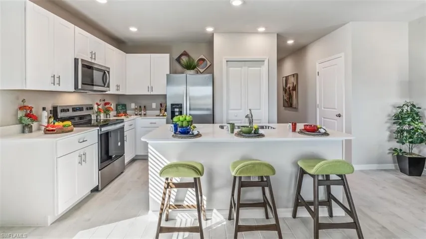 Kitchen featuring white cabinetry, an island with sink, appliances with stainless steel finishes, and a kitchen breakfast bar