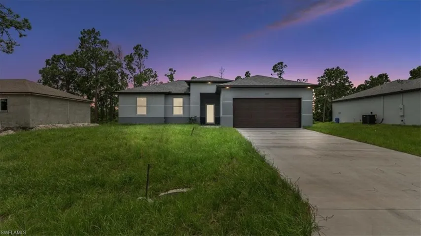 View of front of property with stucco siding, concrete driveway, a front lawn, and an attached garage