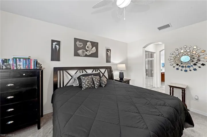 Carpeted bedroom with arched walkways, a ceiling fan, and ensuite bathroom