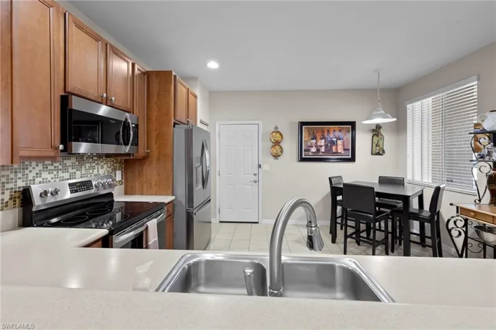 Kitchen featuring appliances with stainless steel finishes, brown cabinetry, light countertops, backsplash, and decorative light fixtures