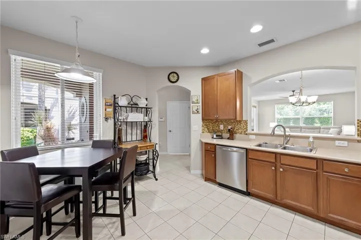 Kitchen featuring arched walkways, brown cabinetry, light countertops, dishwasher, and recessed lighting