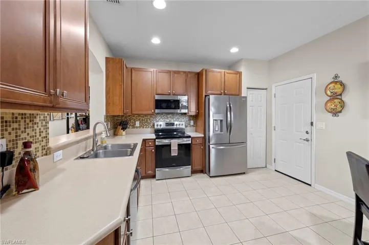 Kitchen featuring tasteful backsplash, appliances with stainless steel finishes, light tile patterned floors, light countertops, and brown cabinetry
