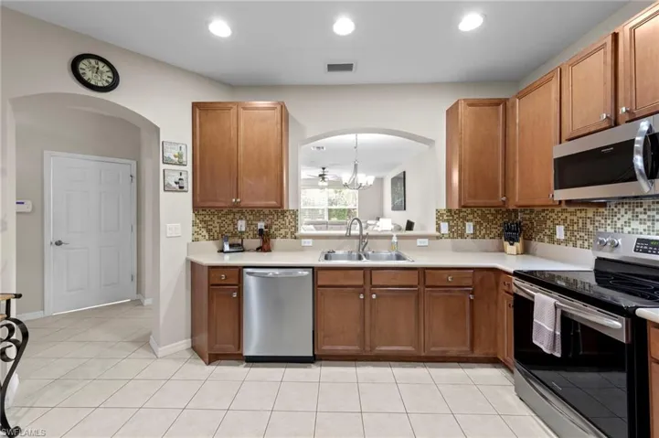 Kitchen with tasteful backsplash, appliances with stainless steel finishes, arched walkways, light countertops, and brown cabinetry