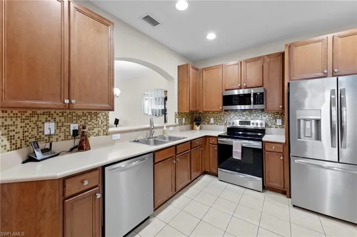 Kitchen featuring decorative backsplash, stainless steel appliances, light countertops, arched walkways, and light tile patterned flooring