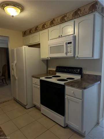 Kitchen featuring fridge, white cabinetry, white stove, and light tile flooring