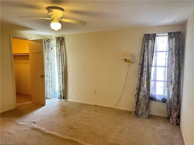 Unfurnished primary bedroom featuring carpet flooring, a walk in closet, and ceiling fan