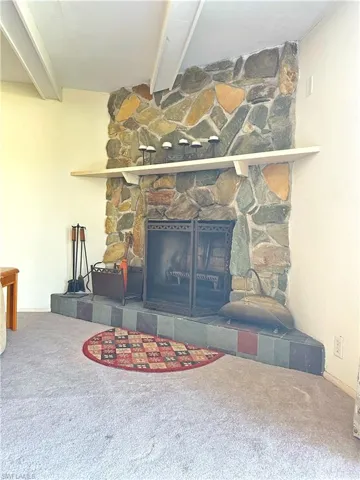 Interior details with carpet, a stone fireplace, and beam ceiling