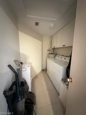 Utility room with separate washer and dryer, light tile flooring, and cabinets