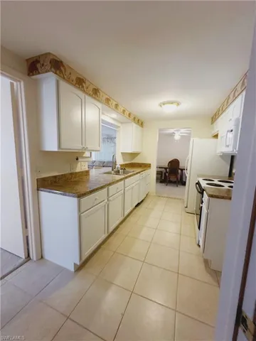 Kitchen featuring sink, light tile flooring, white appliances, and white cabinetry