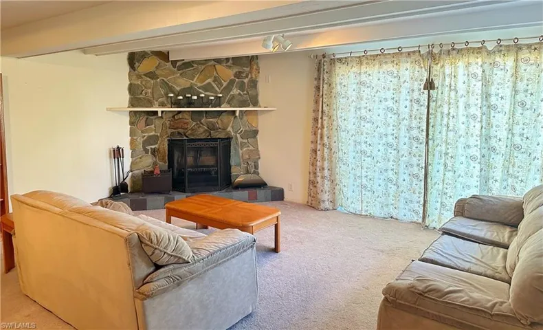 Carpeted living room featuring a stone fireplace and beamed ceiling