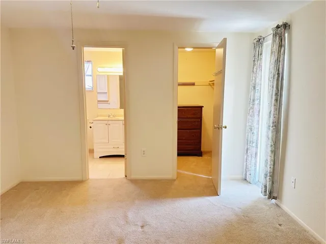 Unfurnished primary bedroom featuring a walk in closet, connected bathroom, sink, a closet, and light colored carpet