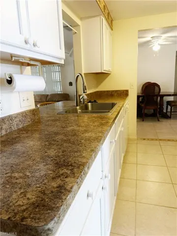 Kitchen featuring white cabinets, sink, ceiling fan, and light tile flooring