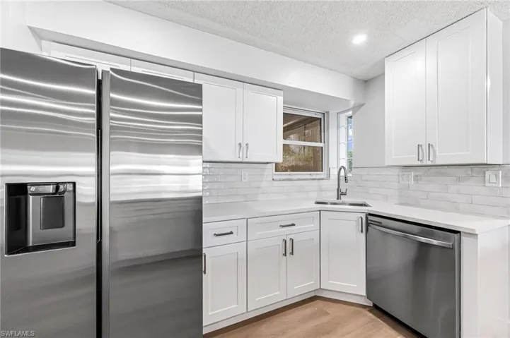 Kitchen with light hardwood / wood-style flooring, tasteful backsplash, sink, white cabinets, and appliances with stainless steel finishes