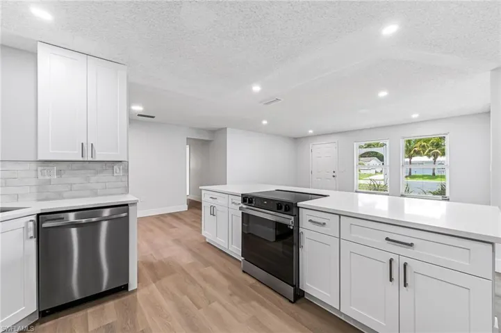 Kitchen with stainless steel appliances, tasteful backsplash, white cabinets, and light wood-type flooring
