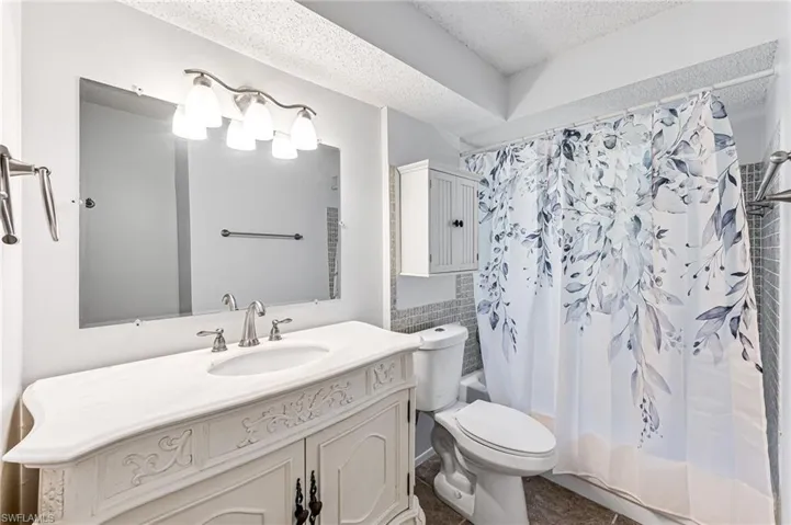 Full bathroom with tile flooring, toilet, a textured ceiling, shower / bath combo with shower curtain, and vanity