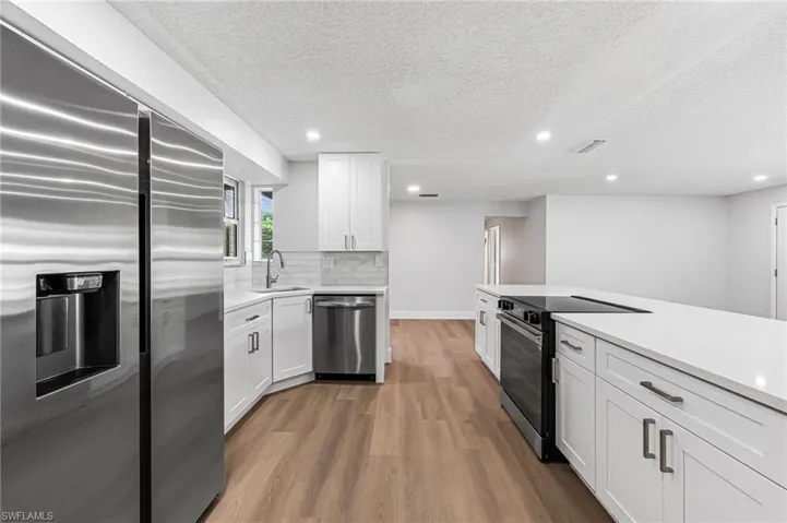 Kitchen with sink, light hardwood / wood-style floors, white cabinetry, and appliances with stainless steel finishes